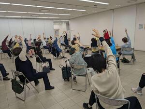 椅子に座って体操を行っている