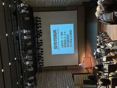 講演会の会場写真です。スライド内容「慢性腎臓病とは、eGFR<60、尿蛋白≧1+、等の異常が3か月以上持続した状態です。」